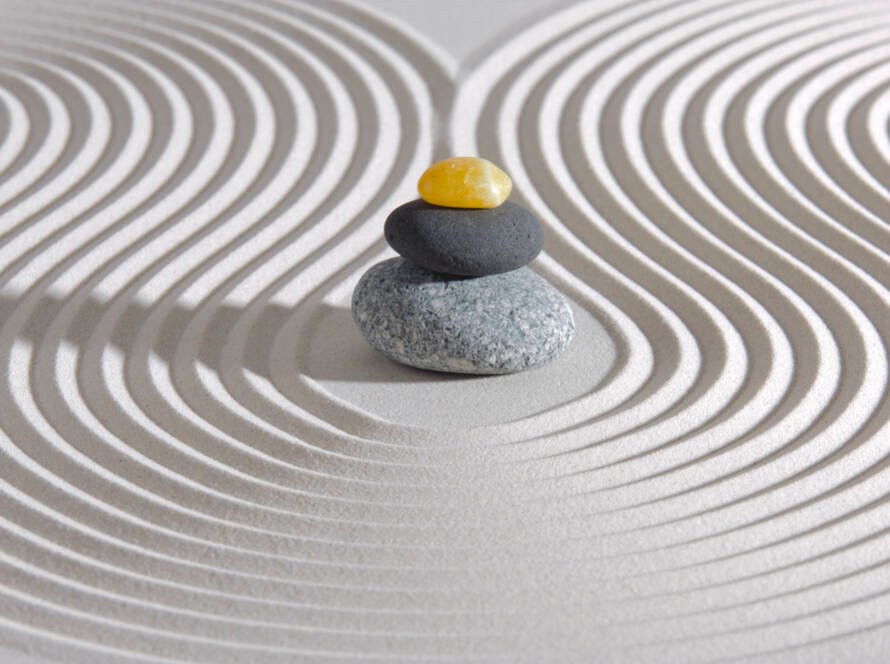 a sand zen garden with lines around a stack of three rocks, a large light gray one, a medium dark gray one, and a yellow citrine on top