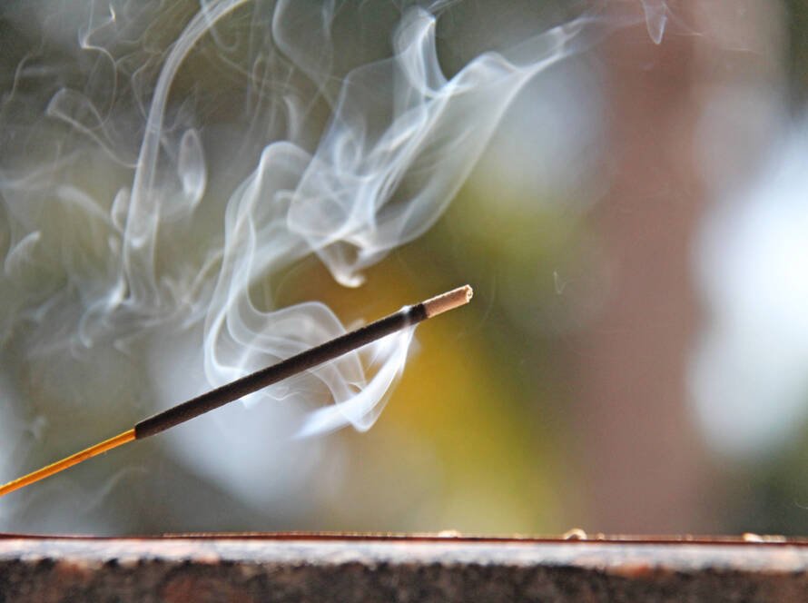 smoke curling from an incense stick burning on a wooden burner in front of a blurred green backdrop